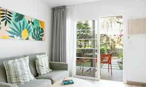 Vardagsrumsmiljö med grå soffa, prydnadskuddar, färgglad väggkonst, och glasdörr som leder till uteplats. (AI-genererad text)