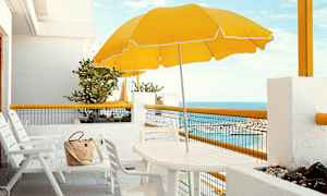 Vit uteplats med stolar, bord, gul parasoll och en havsutsikt. (AI-genererad text)