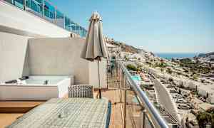 En balkong med sittgrupp och utsikt över en stad och havet. (AI-genererad text)