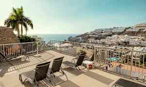 En terrass med solstolar och utsikt över havet och byggnader på en sluttning. (AI-genererad text)