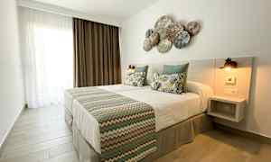 Ett sovrum med en dubbelsäng, prydnadskuddar och en dekorerad huvudgavel. (AI-genererad text)