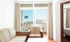 Ett rum med en soffa och en fåtölj klädda i randigt tyg, ett soffbord och en balkong med utsikt mot en byggnad. (AI-genererad text)