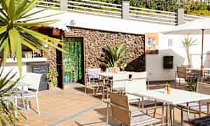 Terrass med bord, stolar och parasoll nära en byggnad med stenfasad. (AI-genererad text)