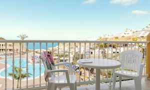 Utsikt från en balkong med vita möbler mot en pool och en havsutsikt. (AI-genererad text)