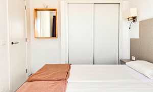 Ett hotellrum med vit inredning, en dubbel säng med vita lakan och bruna överkast, samt en spegel på väggen. (AI-genererad text)