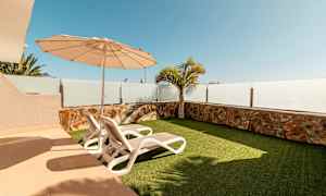 En uteplats med två solstolar, parasoll och konstgräs. (AI-genererad text)