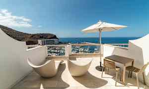 Terrass med utsikt över hamn och hav, utrustad med moderna stolar, bord och parasoll. (AI-genererad text)