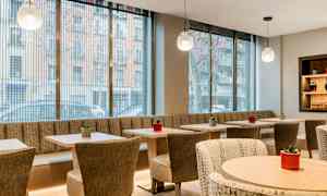 Ett modernt och ljust inrett kafé med stora glasfönster, bord och stolar samt små planteringar som dekoration. (AI-genererad text)