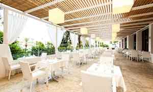 Restaurang med vita bord och stolar under tak nära grönska. (AI-genererad text)