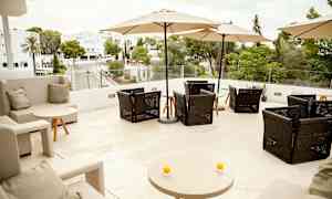 Terrass med sittplatser och parasoller, utsikt över grönska och byggnader. (AI-genererad text)