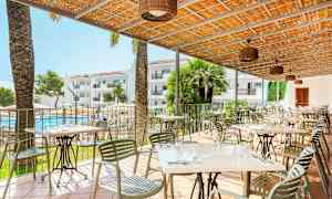 Terrass med bord och stolar, en pool och hotellbyggnader i bakgrunden. (AI-genererad text)