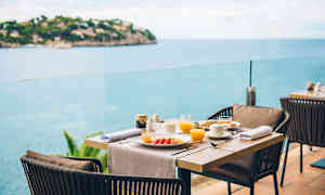 Dukat matbord med tallrikar och glas på en terrass med havsutsikt. (AI-genererad text)