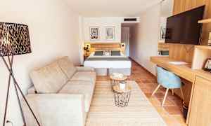 Ett hotellrum med en soffa, en dubbelsäng, ett skrivbord med en stol och en TV. (AI-genererad text)