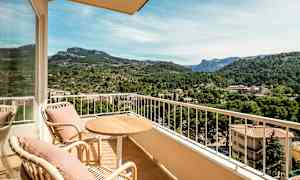 Utemöbler på en balkong med utsikt över en grönskande dal och berg i bakgrunden. (AI-genererad text)