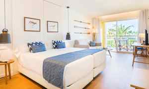 Ett modernt hotellrum med två sängar och blå detaljer samt en balkong med utsikt mot palmer. (AI-genererad text)