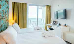 Hotellrum med två bäddar, skrivbord, vägg-TV och utsikt mot havet från balkong. (AI-genererad text)