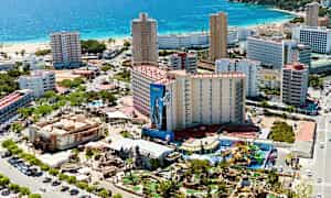 Flygfoto av en kuststad med hotellbyggnader, strand och ett nöjesområde. (AI-genererad text)