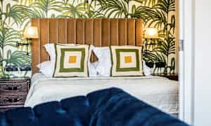 Ett sovrum med en säng, två kuddar och tapet med stora gröna bladmotiv. (AI-genererad text)