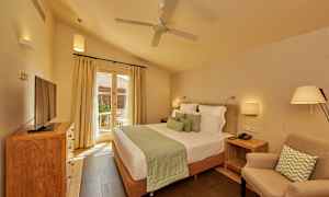 Ett sovrum med en dubbelsäng, en fåtölj, en tv på ett skåp och en dörr med glas som leder ut till en terrass. (AI-genererad text)