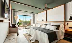 Ett modernt hotellrum med en stor bäddad säng, soffa och ett stort fönster mot en terrass. (AI-genererad text)