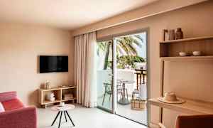 Hotelrum med sittgrupp, TV, bord och balkong med utsikt mot palmer. (AI-genererad text)