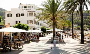 En gata med palmer, bord och byggnaden Marina bredvid en strand. (AI-genererad text)