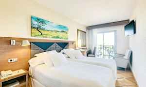 Ett hotellrum med två enkelsängar, ljusa sängkläder, en tavla ovanför huvudgaveln, en liten balkong och en TV på väggen. (AI-genererad text)