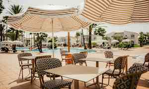 Utomhuspoolområde med solstolar, parasoller och bord med stolar. (AI-genererad text)