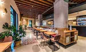 En stilren restaurangmiljö med trädetaljer i taket, bekväma stolar och bord, samt dekorativa växter. Ett barområde syns i bakgrunden. (AI-genererad text)