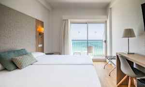 Hotellrum med två sängar, skrivbord och utsikt över havet genom en glasdörr. (AI-genererad text)