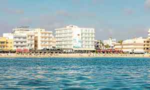 Vy från havet mot en strand med flera byggnader och människor som solar. (AI-genererad text)