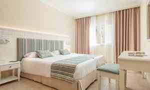 Hotellrum med en dubbelsäng, ljusa färger och ett fönster med gardiner. (AI-genererad text)