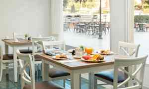Ett dukat bord med frukostmat, inklusive juice, bröd och frukt, i en ljus matsal med fönster som vetter mot en utomhusterrass. (AI-genererad text)