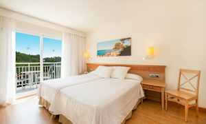 Ett hotellrum med två enkelsängar, en balkong och ett landskapsfoto på väggen. (AI-genererad text)