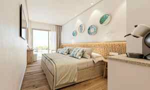 Ett modernt hotellrum med en dubbelsäng, dekorativa prydnadsskålar på väggen, en kaffemaskin och stora glasdörrar som leder till en balkong. (AI-genererad text)