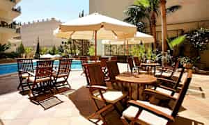 Utomhusområde med trädgårdsmöbler i trä runt ett poolområde med parasoller och växter. (AI-genererad text)