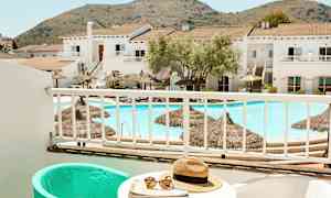 Utsikt från en balkong mot en pool och byggnader med berg i bakgrunden. (AI-genererad text)