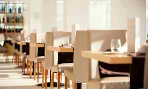 Interiör av en ljus och elegant restaurang med dukade bord och stolar. (AI-genererad text)