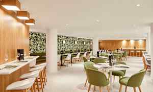 En restauranginteriör med grönmålade stolar och ett tapetserat väggmönster med växtmotiv. (AI-genererad text)