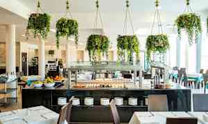 Restaurang med bord, stolar och buffé samt hängande gröna växter. (AI-genererad text)