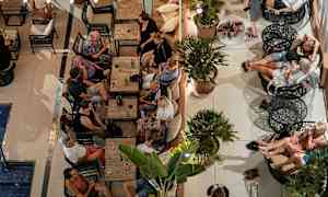 En grupp människor sitter vid bord och soffor i en utomhuslounge. (AI-genererad text)