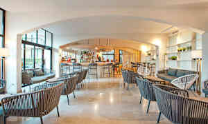 Interiör av en modern lounge med bar, där flera sittgrupper är uppställda med stolar och soffor i ett ljust och luftigt rum. (AI-genererad text)