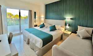 Ett hotellrum med en dubbelsäng, en soffa, ett skrivbord och ett fönster med utsikt över grönska. (AI-genererad text)