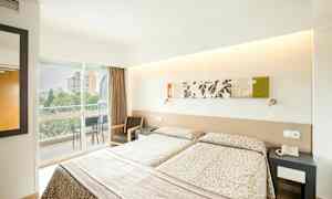 Ett hotellrum med två enkelsängar, dekorerade med mönstrade överkast. Det finns en möblerad balkong som vetter mot utomhusområdet. (AI-genererad text)