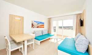 Vardagsrum med två blå soffor, ett bord och stolar, samt en balkong med utsikt. (AI-genererad text)