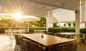 Utomhusrestaurang med solens strålar genom parasoller och grönska. (AI-genererad text)