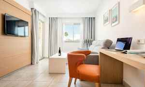 Ljust, modernt hotellrum med soffa, stol, TV, skrivbord och stora fönster. (AI-genererad text)