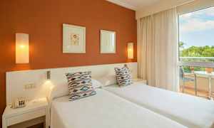 Bild av ett hotellrum med två enkelsängar, prydnadskuddar, konst på väggen och en balkong med utsikt. (AI-genererad text)