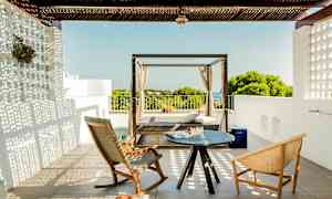 En terrass med två stolar och ett litet bord samt en dagbädd med utsikt över grönska och hav. (AI-genererad text)