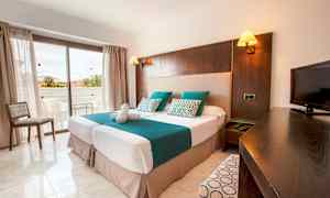 Ett hotellrum med två enkelsängar, en TV och en balkong i bakgrunden. (AI-genererad text)